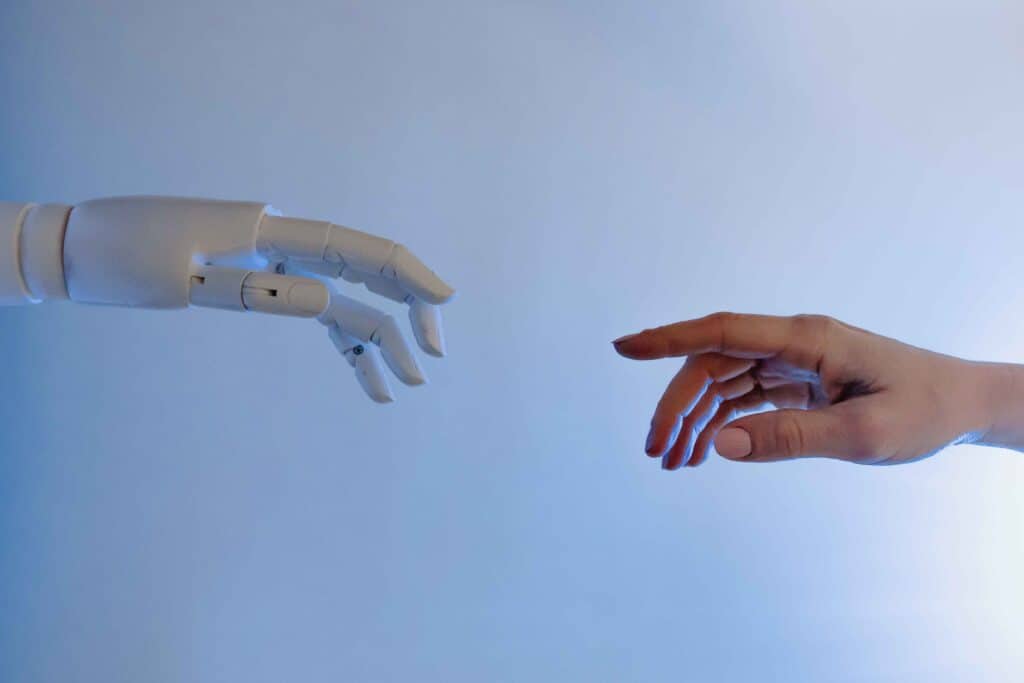 A robot hand reaching out to touch a human hand to represent AI recruitment tools helping to source candidates for job roles.