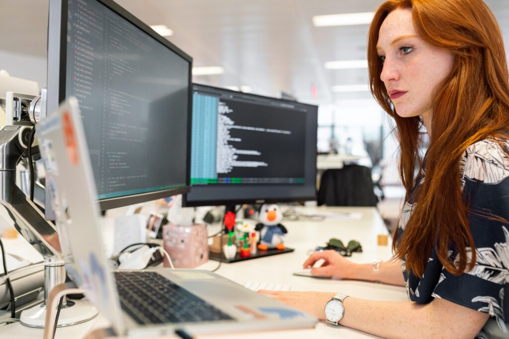 A image a woman, who is a Creator of blockchains sitting at a desk working with two computer screens and a laptop.